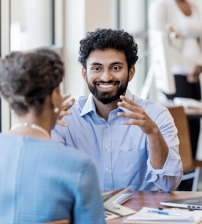 Man sitting at desk smiling and explaining to women across from him 