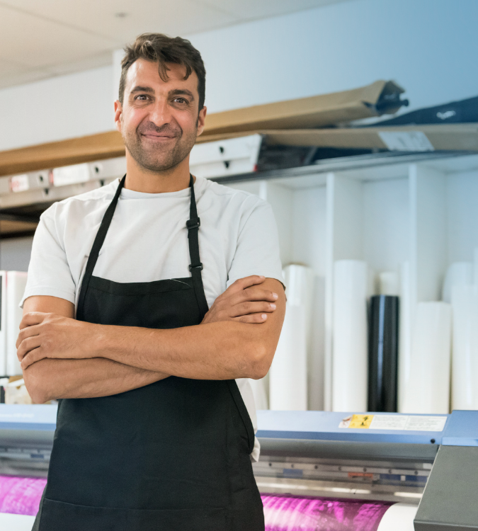 Man with apron standing in front of industrial ink roller 