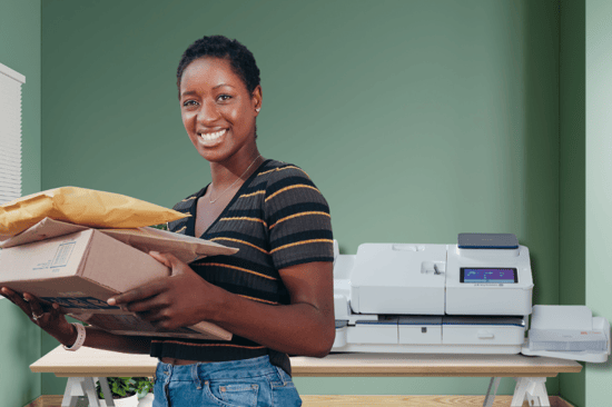Woman holding packages in front of Pitney Bowes SendPro postage meters